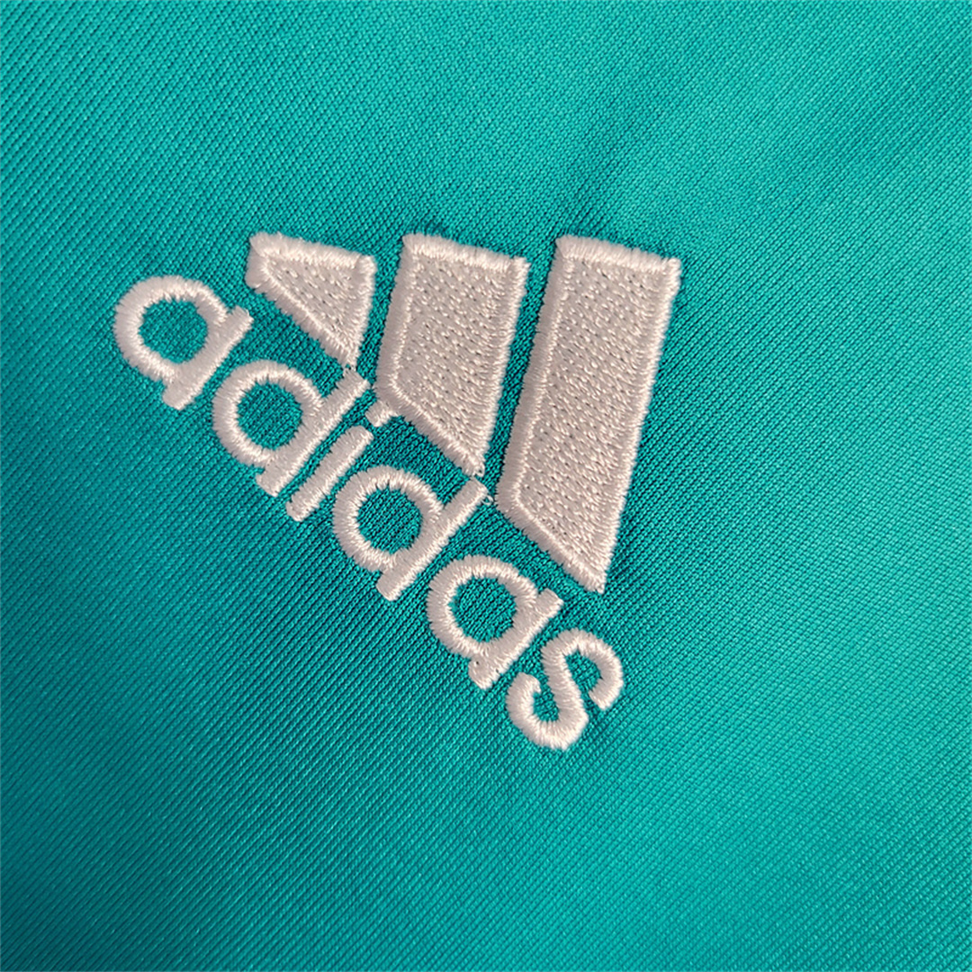 Dettaglio_ravvicinato_dello_stemma_del_Adidas_ricamato_in_bianco_su_tessuto_turchese.png