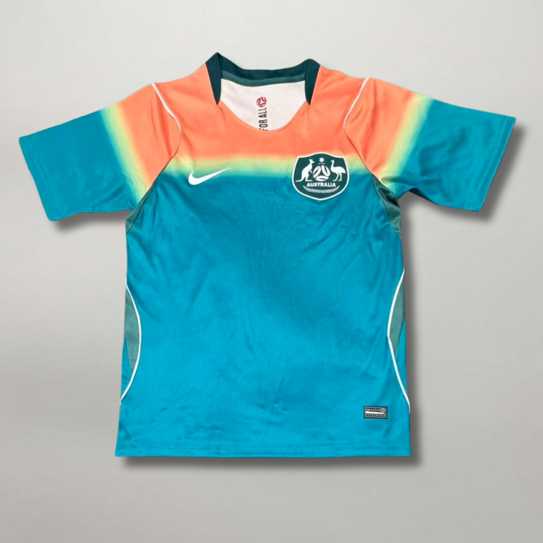 Fronte_della_maglia_away_dell_Australia_2026_turchese_con_spalle_sfumate_oro_e_arancione_e_stemma_sul_petto.png