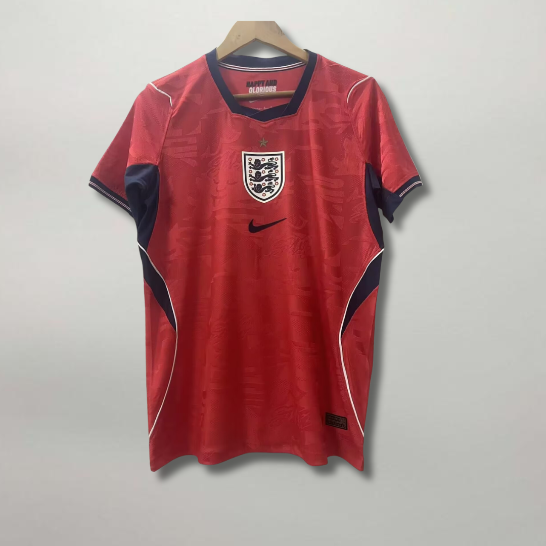 Fronte_della_maglia_away_dell_Inghilterra_2026_scura_con_dettagli_geometrici_colorati_sui_fianchi_e_stemma_ricamato.png