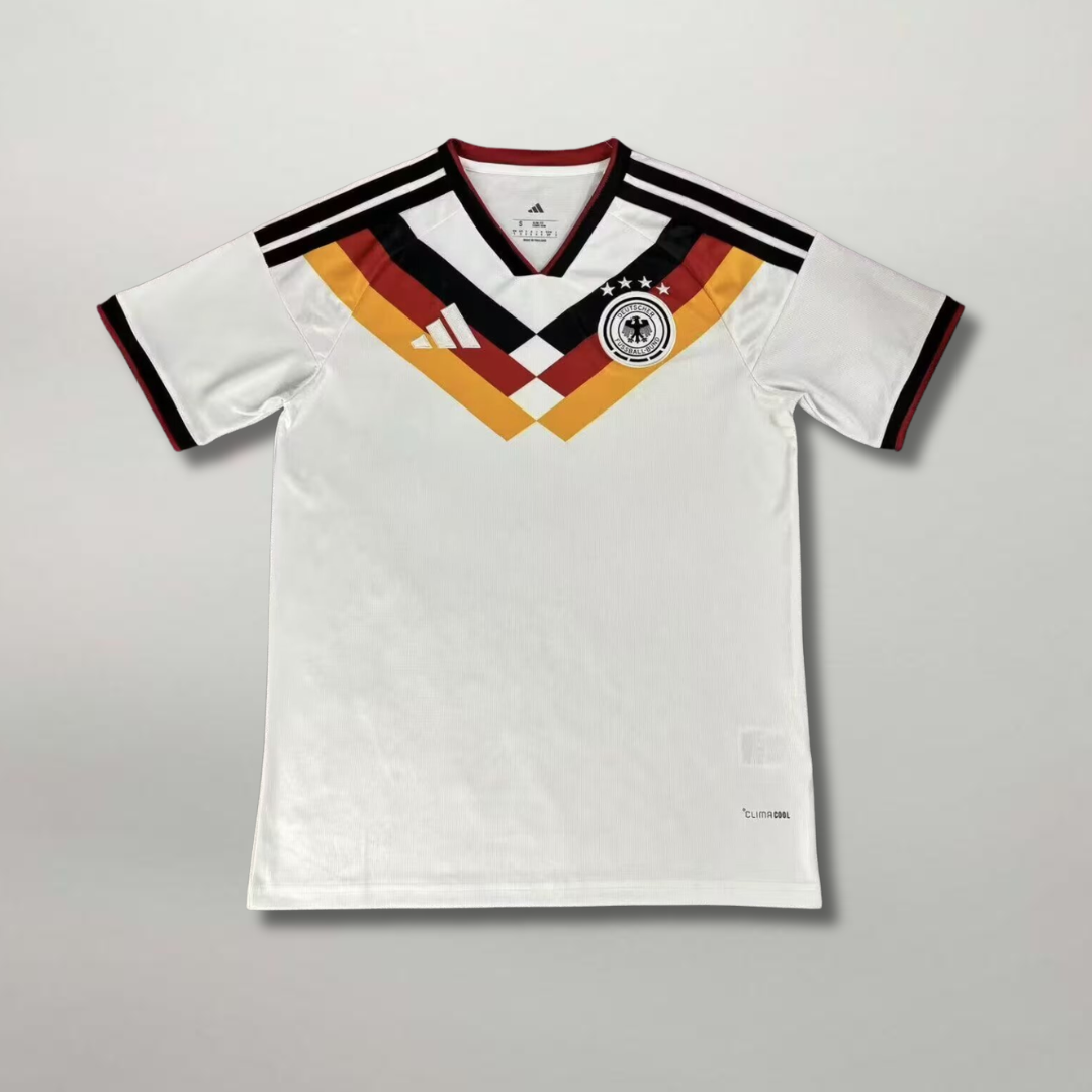Fronte_della_maglia_home_della_Germania_2026_bianca_con_motivo_geometrico_nero_rosso_oro_sul_petto_e_stemma_centrale.png